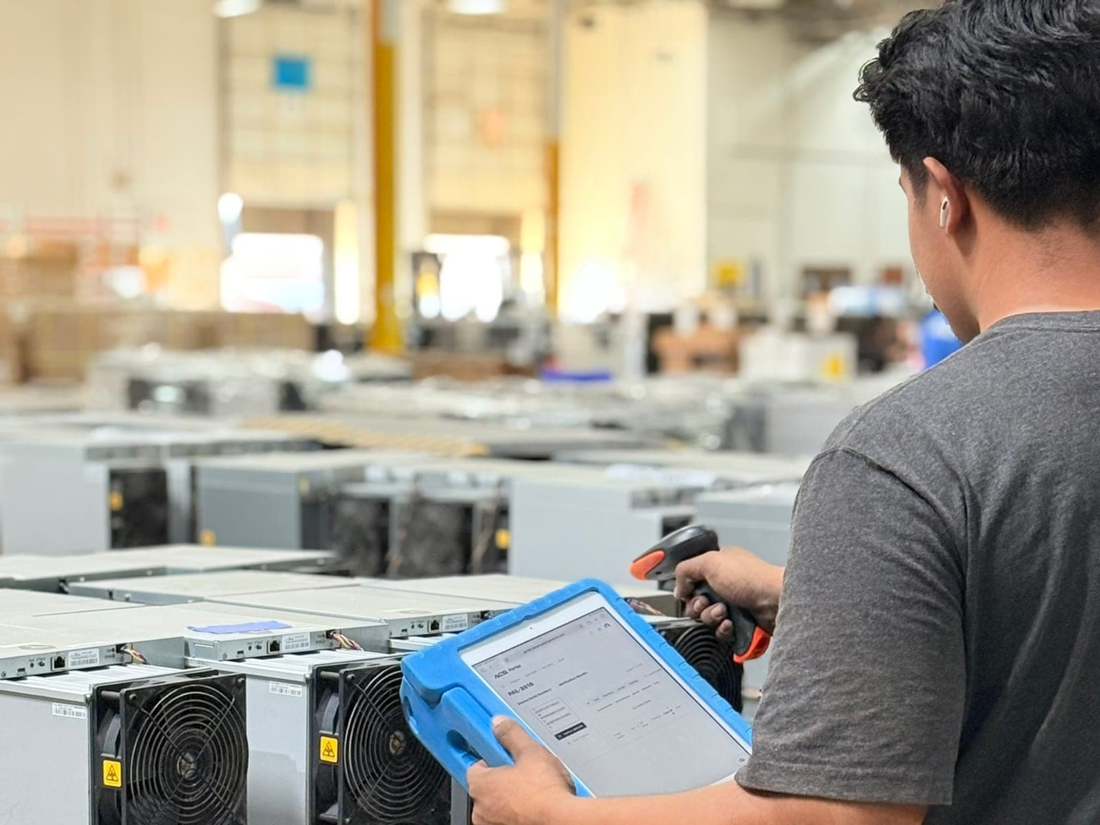 A technician logging a miner on a rugged tablet at the ACS inspection benches